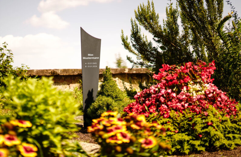 Moderne Grabstele aus Aluminium mit individueller Lasergravur auf blühendem Friedhof
