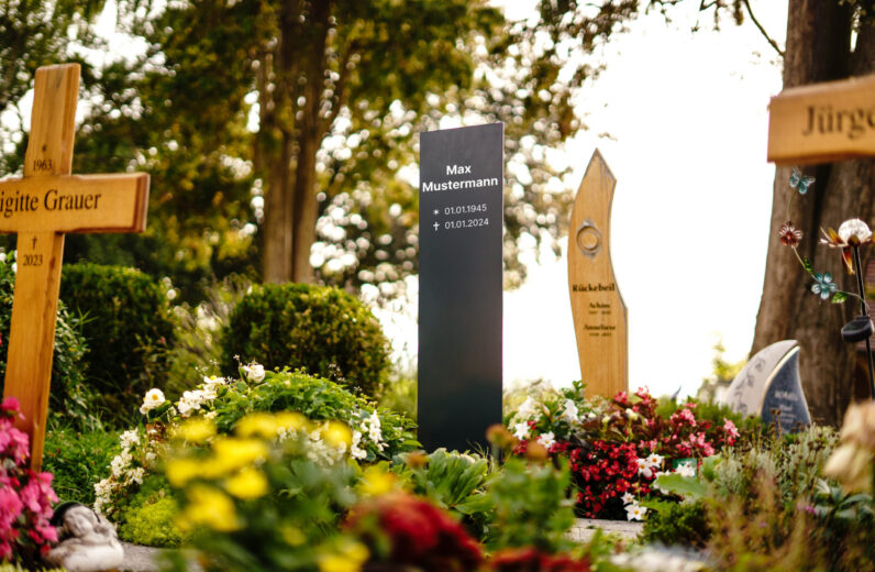 Schlichte Aluminium Grabstele mit Lasergravur auf bepflanztem Friedhof